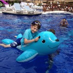 Boy riding floating blue seal raft in swimming pool