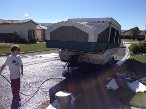 boy washes tent trailer with hose